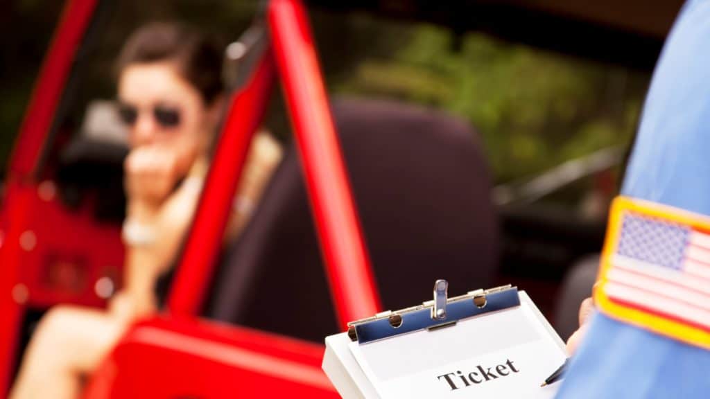 Caucasian female in red vehicle getting a ticket from a policeman.